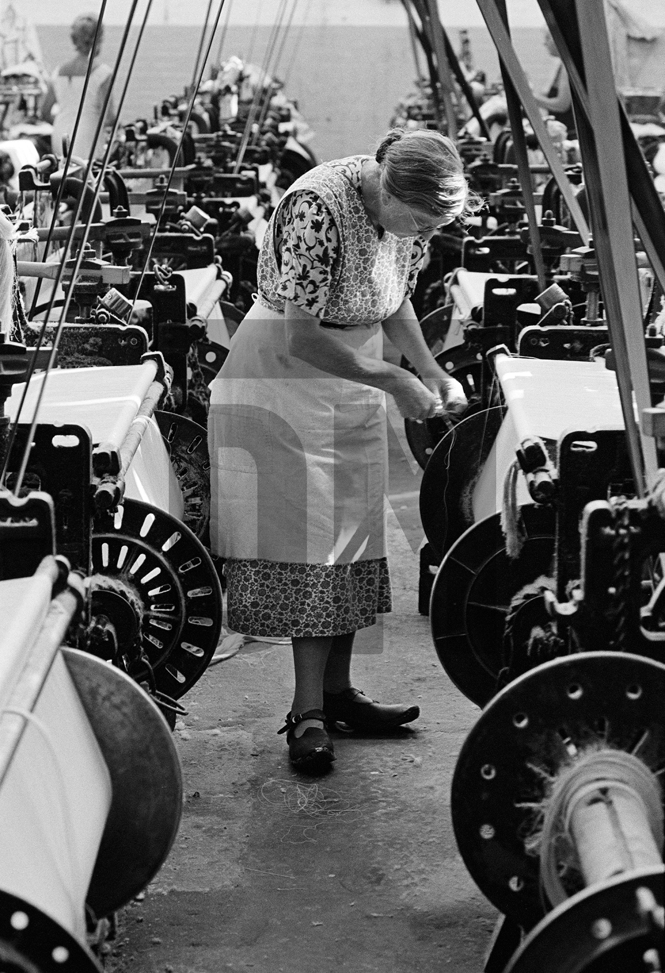 Weaver in ‘brat’ (apron) and clogs, Queen Street Mill, Harle Syke, Burnley, Lancashire. July 1976 by Daniel Meadows