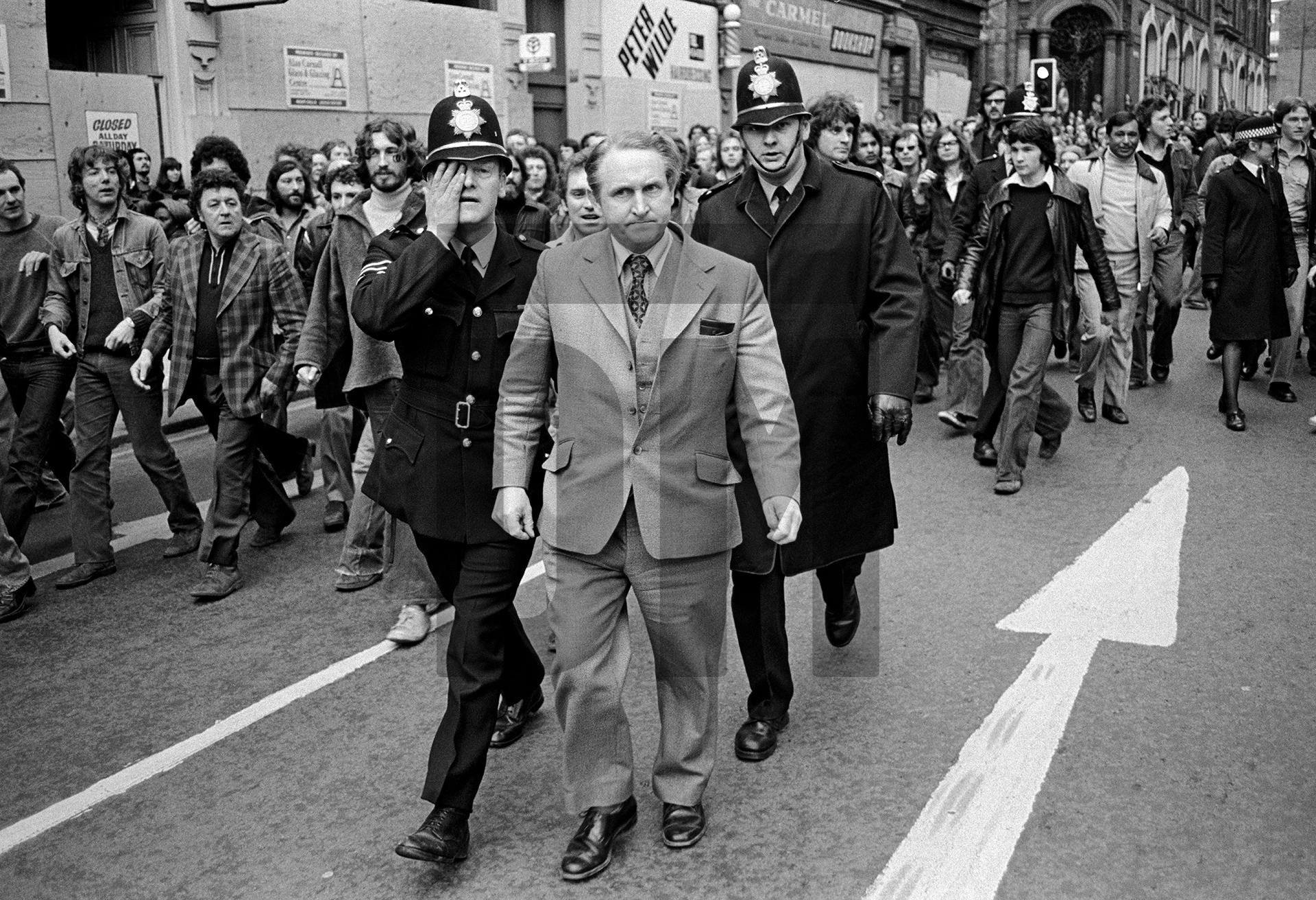 Anti Nazi League (ANL) demonstration against a National Front (NF) meeting. George Wright, NF Parliamentary candidate for Rotherham in the 1976 by-election (1,696 votes), is escorted by police through demonstrators, policeman wiping spittle from his face, Leeds. April 1978 by Daniel Meadows